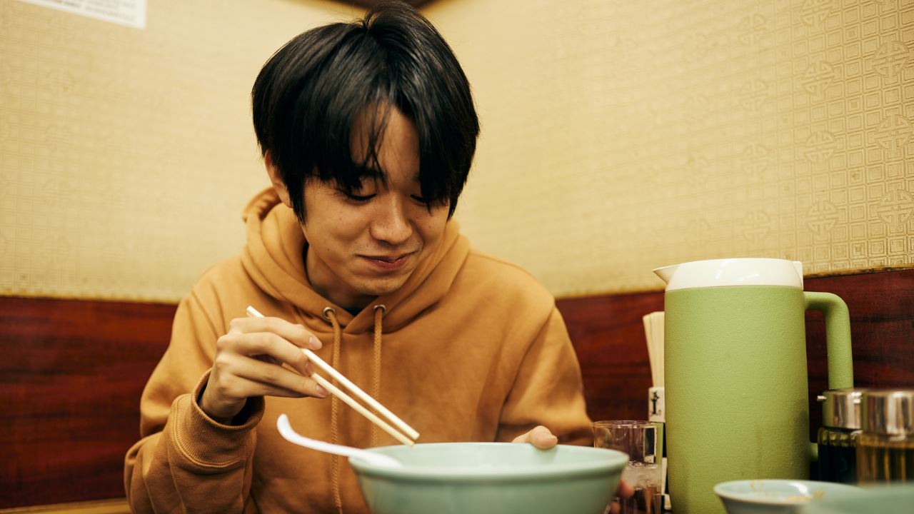 Asian man holding chopsticks and eating noodles from a bowl