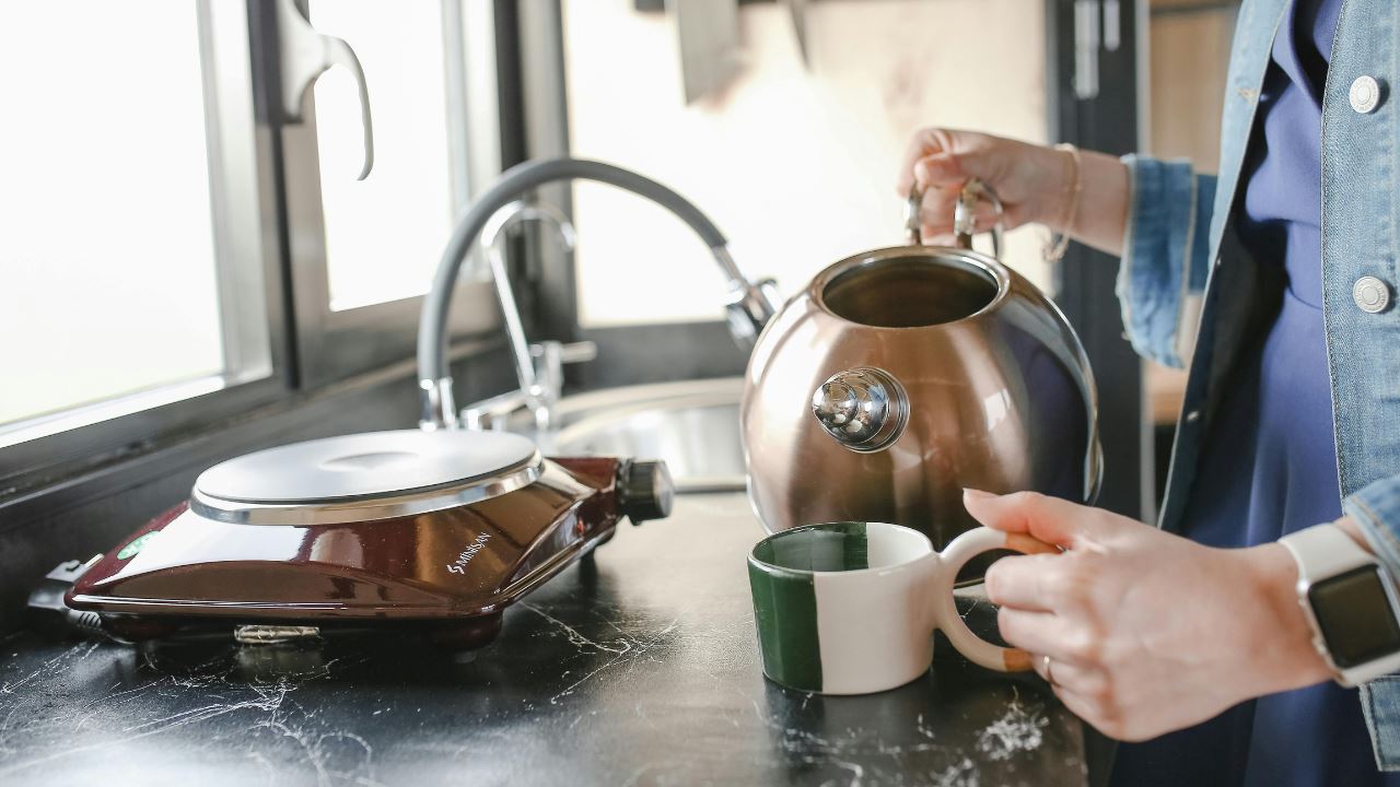 Someone pouring water from a steel kettle into a cup.