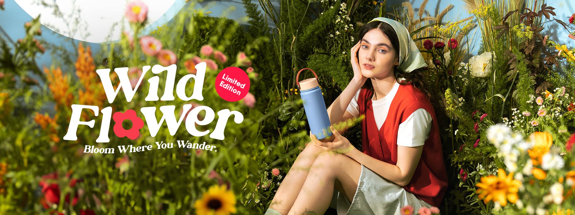 A girl sitting in a flower field holding a tumbler